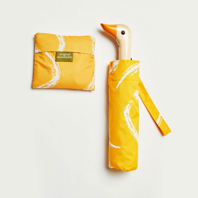 Yellow duck-shaped umbrella with matching tote bag on a light gray background