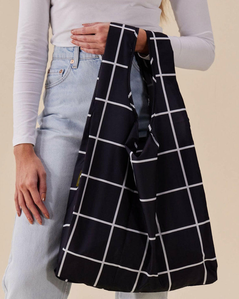 Person holding a black and white grid-patterned bag against a beige background