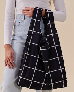 Person holding a black and white grid-patterned bag against a beige background