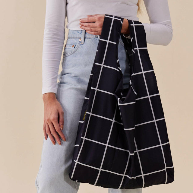 Person holding a black and white grid-patterned bag against a beige background