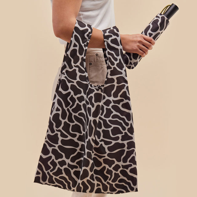 Person holding a tote bag with black and white ripples pattern, holding an umbrella against a beige background