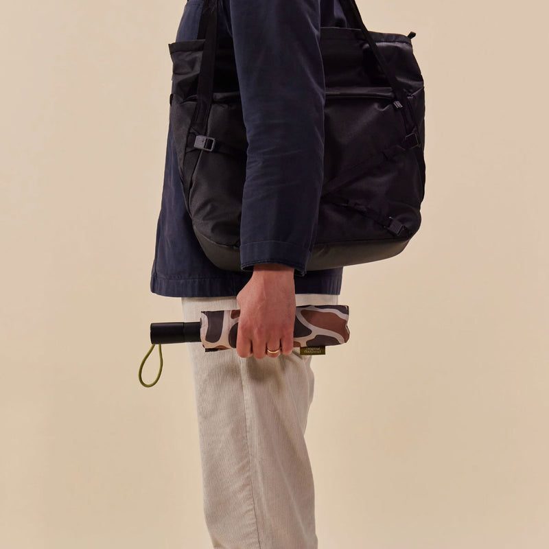 Person holding a black backpack and a patterned umbrella against a beige background