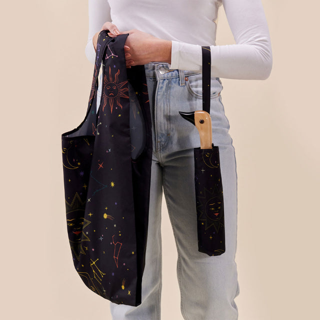 Person holding a black tote bag with celestial design against a beige background with matching umbrella