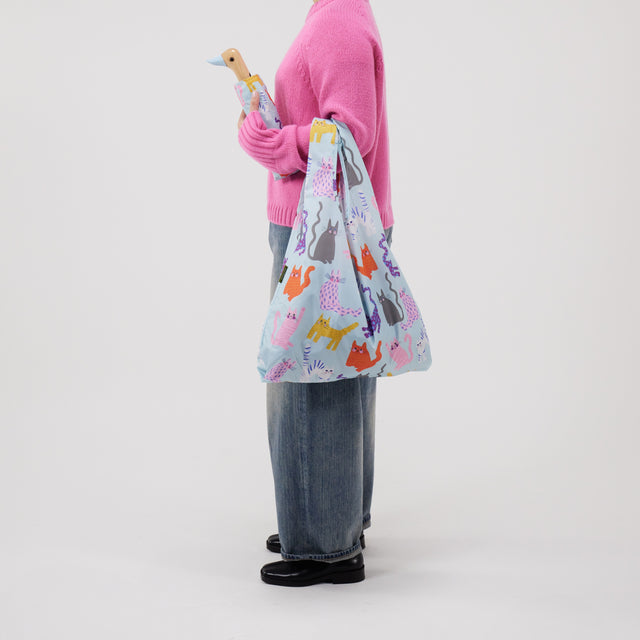 Person holding a colorful reusable bag with cat patterns on a plain background