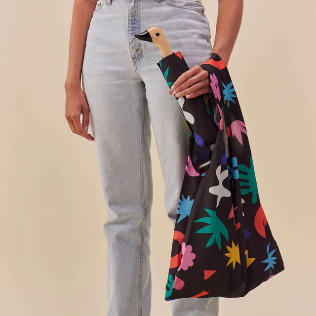 Person holding a colorful bag with a black handle against a beige background