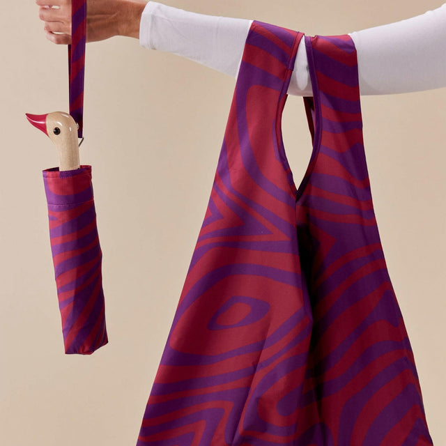 Pink and purple striped bag with matching umbrella held by a person against a beige background