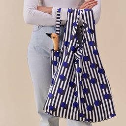 Person holding a striped umbrella with blue polka dots against a beige background