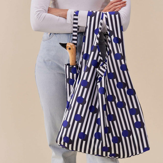 Person holding a striped umbrella with blue polka dots against a beige background