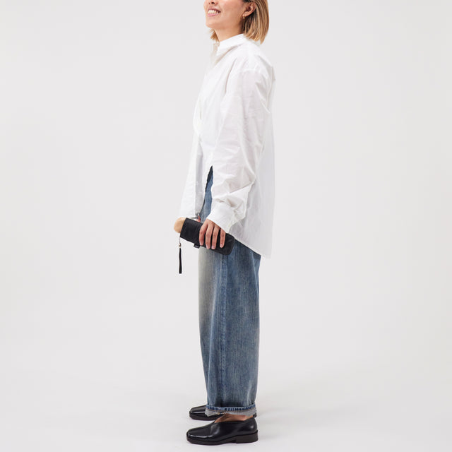 Person wearing a white shirt and blue jeans holding a closed mini black umbrella on a white background