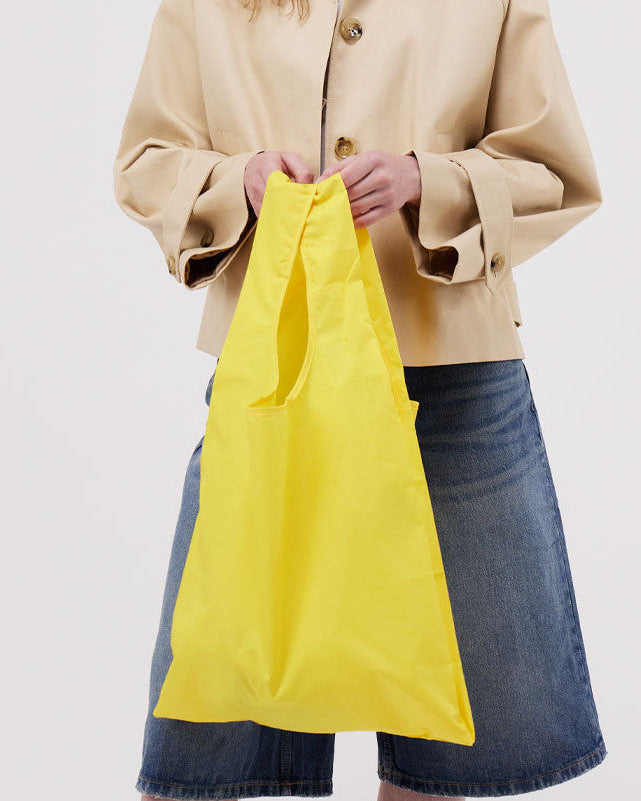 Woman holding a yellow bag wearing a beige jacket and denim skirt on a white background