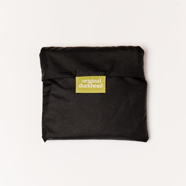 Folded black reusable tote bag in pouch flatlay
