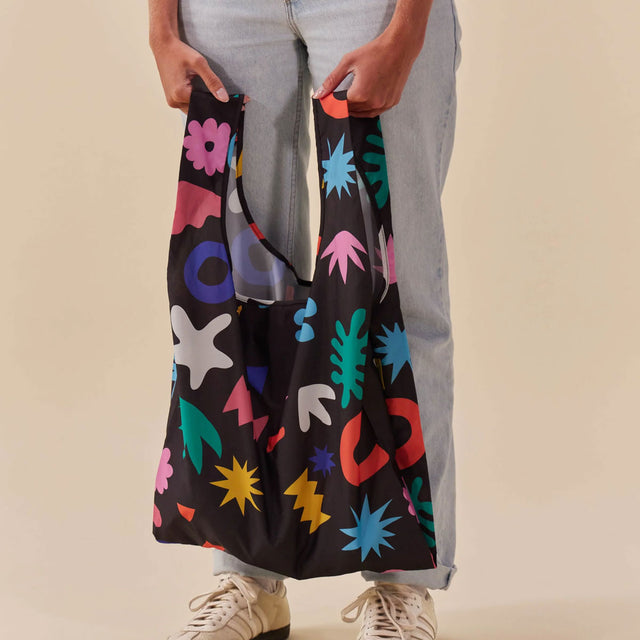 Person holding a colorful reusable bag with abstract patterns on a beige background